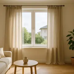 Jasne zasłony wiszą na karniszu po obu stronach okna, za którym widać dom i drzewa.